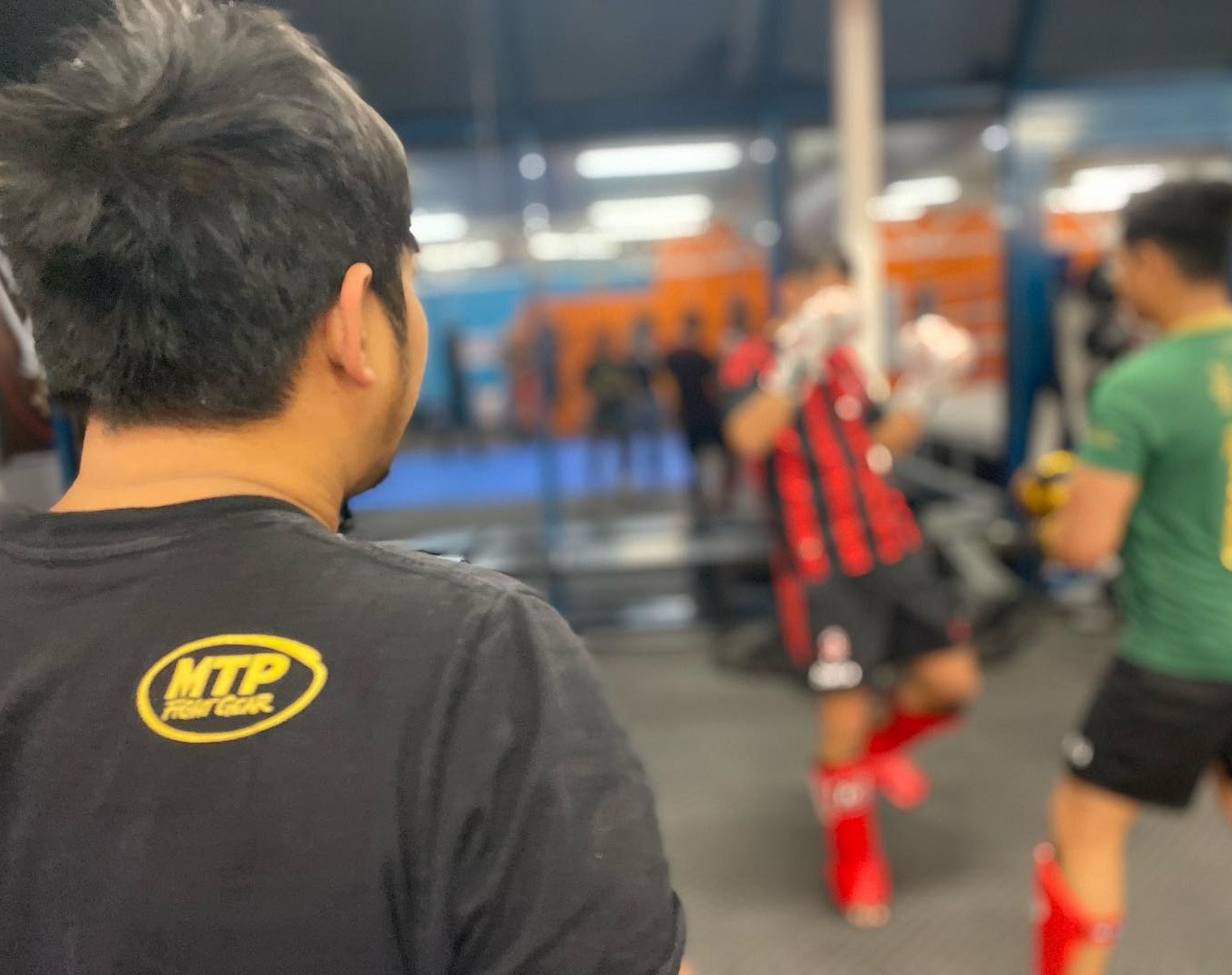 Bilde av baksiden av et medlem som observerer to medlemmer som trener thaiboksing.